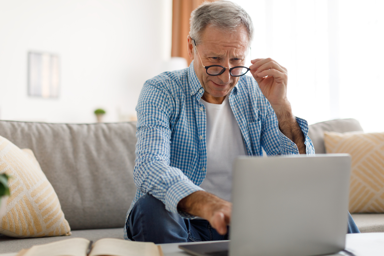 Mature man squinting using laptop, looking at screen