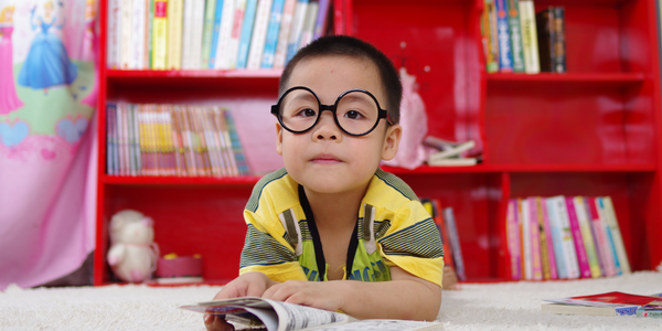 young kid wearing eye glasses, reading a book