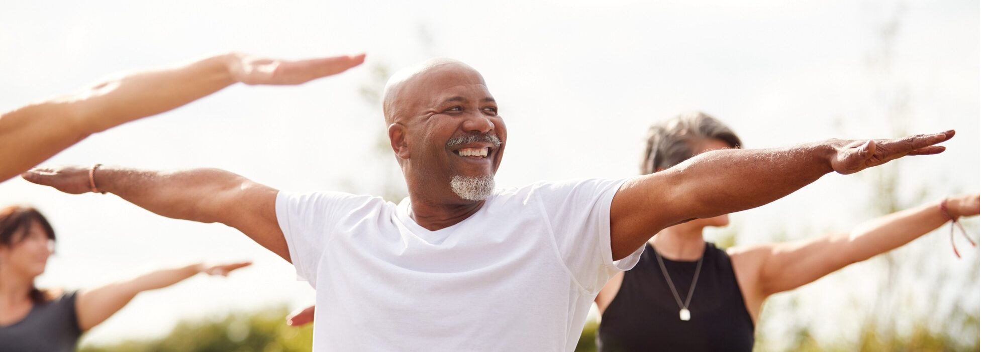 A smiling, middle aged African American man performs yoga in a park.