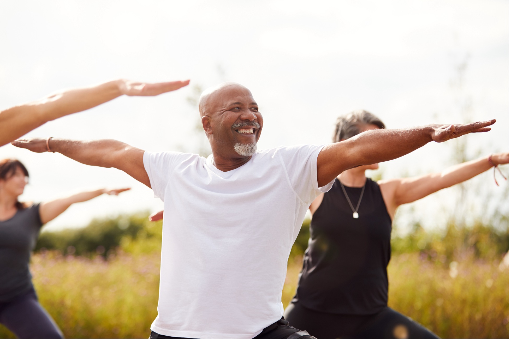 A smiling, middle aged African American man performs yoga in a park.